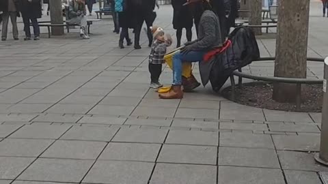 Toddler grooves to the beat of street drummer's performance