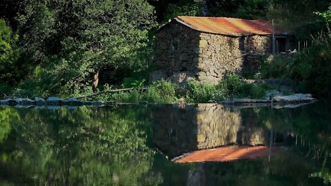 Gentle summer rain hitting a calm lake, by a stone house
