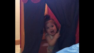 Adorable baby girl plays peek-a-boo with mom
