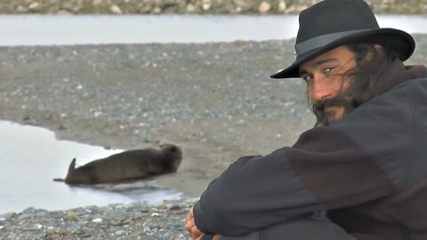 Man in Hat Watching Otter on the Beach