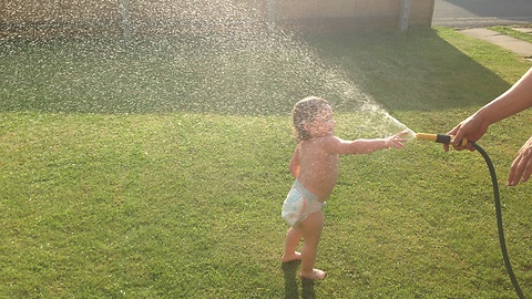 Cute toddler has fun cooling down in the sun with a hosepipe
