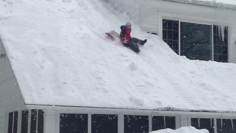 "A Young Boy Slides Off A Roof And Falls In A Large Snow Pile"
