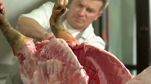 Worker cutting a raw pork at meat factory Processing of meat carcass at slaughterhouse close up