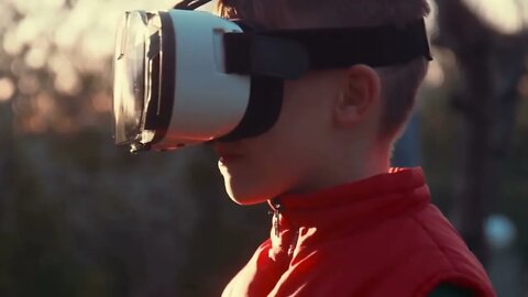 Little boy with surprise and pleasure uses virtual reality helmet and moves around itself outdoor