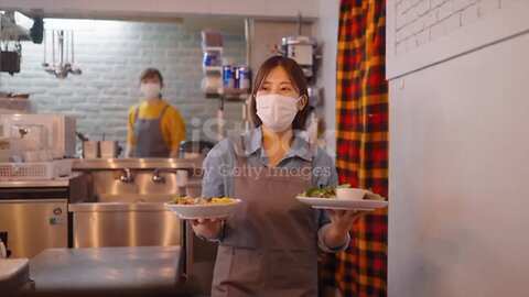 A waitress with a protective face mask is serving food to customers in a café.