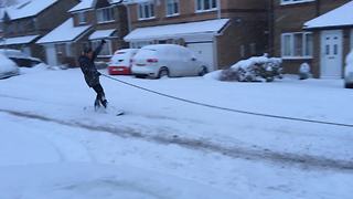 Dude snowboards from back of car through snowy streets