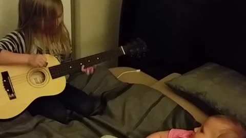 Little girl plays guitar for baby sister
