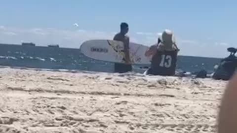 13 jersey guy taking picture of friend holding surfboard on beach