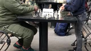 Little boy playing chess in park against man in green track suit