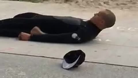 Guy surfer on beach stretching with legs folded back on sidewalk