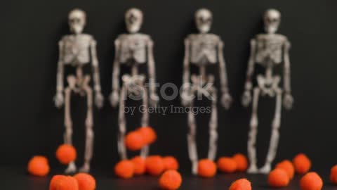 Small orange balls are falling against the background of four skeletons in blur