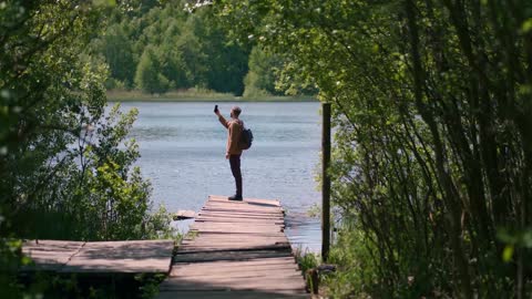 brave man taking photograph in forest lake with smartphone photographing scenic landscape