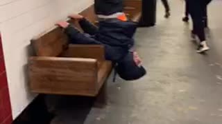 Guy hangs upside down on subway station bench