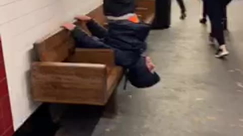 Guy hangs upside down on subway station bench