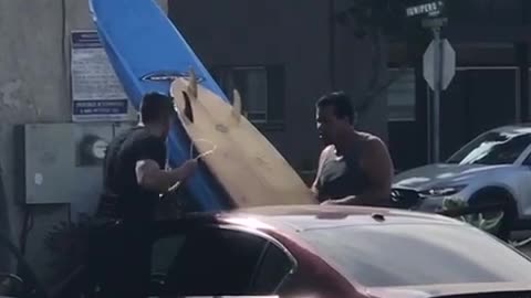 Two men put two surf boards through sunroof of red car