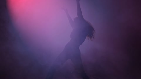Young woman dancing under a cloud of smoke and a purple light