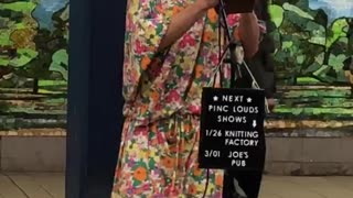 Man in floral dress wig and makeup sings in a subway station