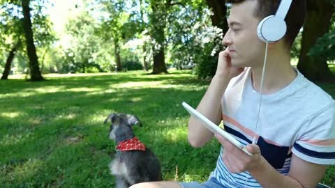 Happy boy listening music while relaxing in the park with his dog, steadycam sho