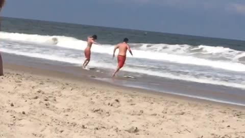 Guy red swim shorts goes into water with friend faceplants into sand water beach
