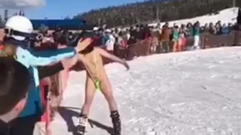 Guy skis down slope and jumps off ramp in mankini sling swimsuit