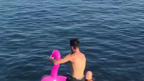 Guy front flip fail off rocks into pink flamingo floatie water