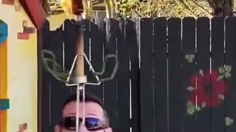 Guy Balances Flaming Wand Over Sword in His Mouth After Popping Balloon in Between