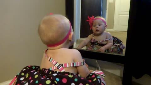 The baby try to talk her self in the mirror