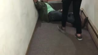 Guy in green shirt and green jacket falls backwards and hits his head on stairs