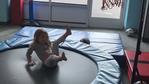 Little girl shoots basketball into hoop while on trampoline and falls back