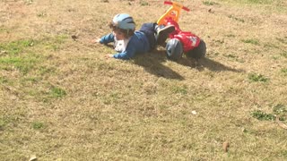 Little kid riding yellow red bike down grass hill falls off