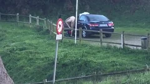 Naked man changing next to black car