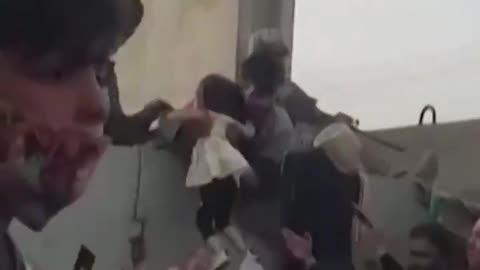 A little Afghan girl is lifted over the wall to U.S. soldiers amid chaos and crowds Kabul airport.