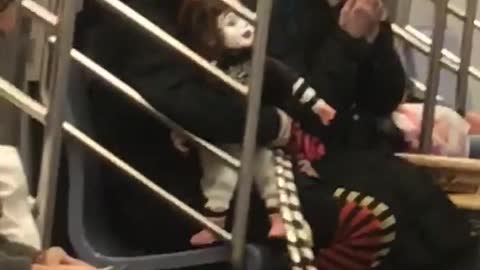 Guy smiles at camera, people dressed as circus clowns sit in the background on subway train