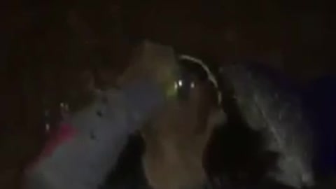 Guy in a club with gold hat and black sunglasses cracks beer over head chugs it