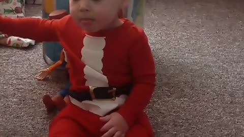 Toddler adorably unaware of unwrapped Christmas gifts directly behind him