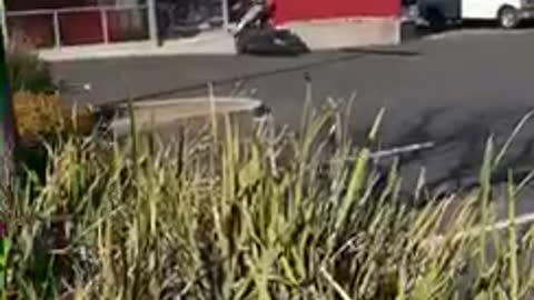 Guy does a wheelie on his motorcycle in a parking lot and crashes into motorcycle store wall