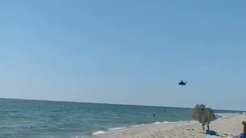 Na pláži Azovského moře lidé mávají ruským vrtulníkům letícím na frontu