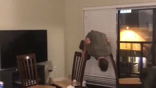 Guy in green shirt tries to do balanced handstand between two chairs falls forward