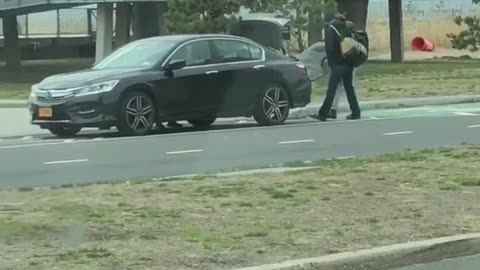 Two guys attempt to put surfboard in trunk of car