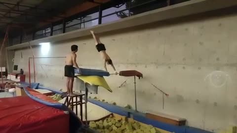 Guy doing flips on pole above yellow foam pit misses flip and hits back on blue cushion