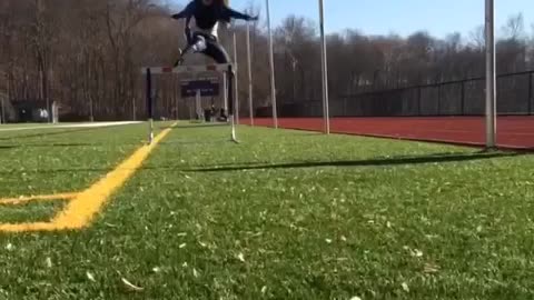 Slo-mo video girl jumps over hurdle, trips over it, and falls down