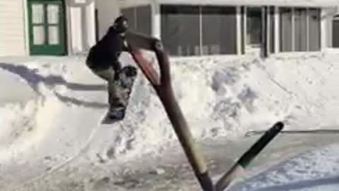 Snowboarder pulled by snow sled, jumps off ramp onto roof and falls