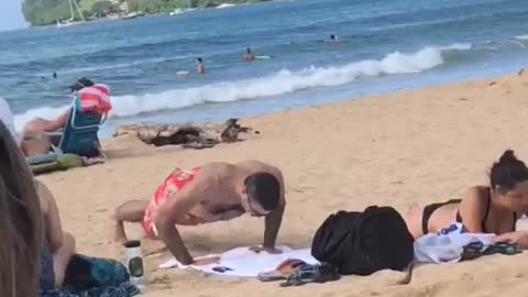 Man in red swim shorts push ups on beach
