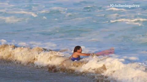 Girl pink surfboard blue bikini running out of water from wave gets knocked over