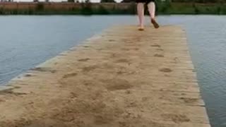 Guy red shirt runs on wooden dock to end and falls in to water lake