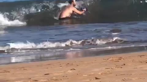 Man trying to take photo in water at beach gets knocked over by wave