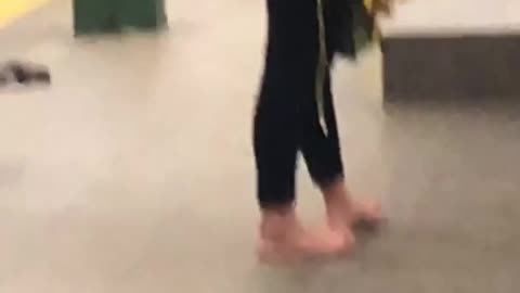 Girl stands inside subway station with no shoes