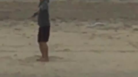 Guy black hat grey sweater arms out spinning in circles on beach sand