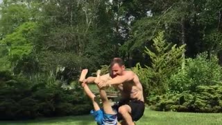 Father and son hold onto each other and roll on grass lawn
