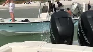 Girl revs boat engine sprays water on shirtless guy on other boat